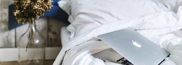 kaboompics_An ornamental golden plant in a jar by the bed with white sheets and a laptop